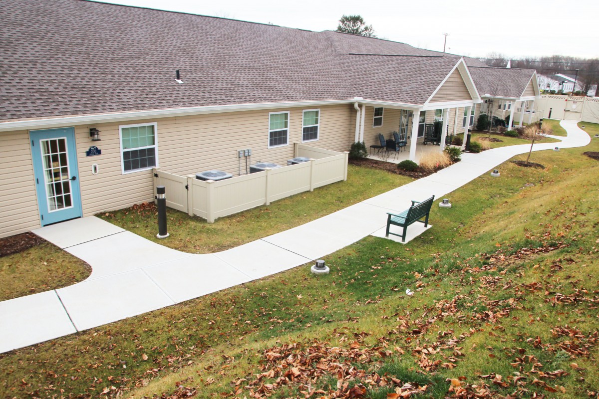 A residential building with a pathway and bench surrounded by a lawn.