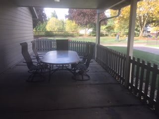 An outdoor patio with a table and chairs, surrounded by a fence in a backyard setting.