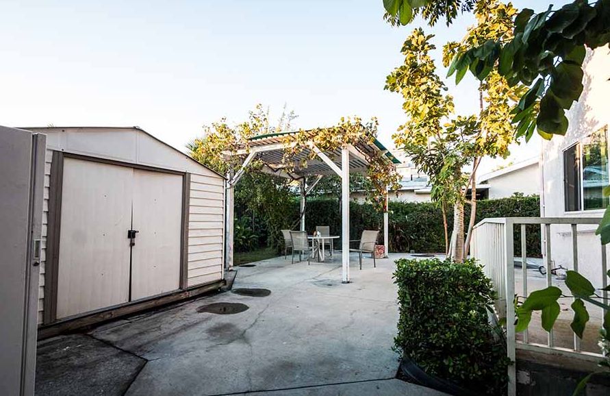 A peaceful backyard with a pergola, patio furniture, and a shed surrounded by trees.