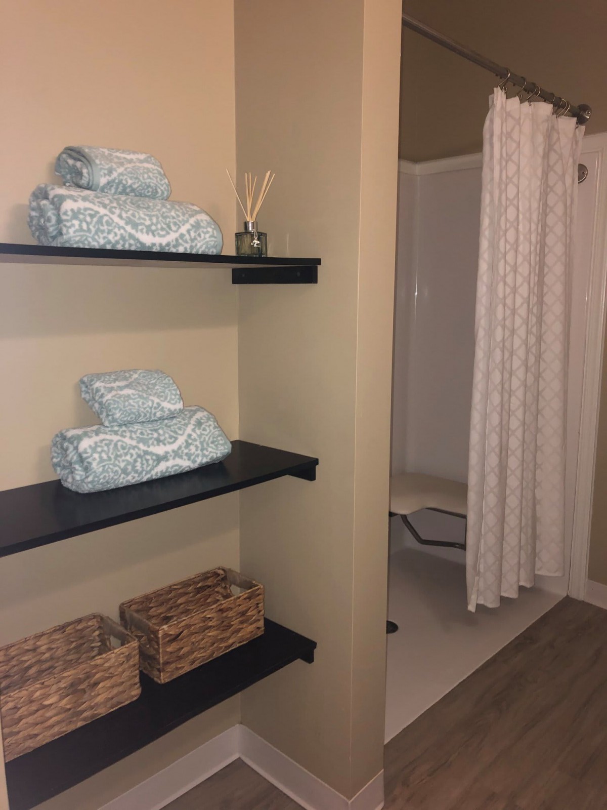 A neatly organized bathroom with shelves holding towels and baskets alongside a shower area.