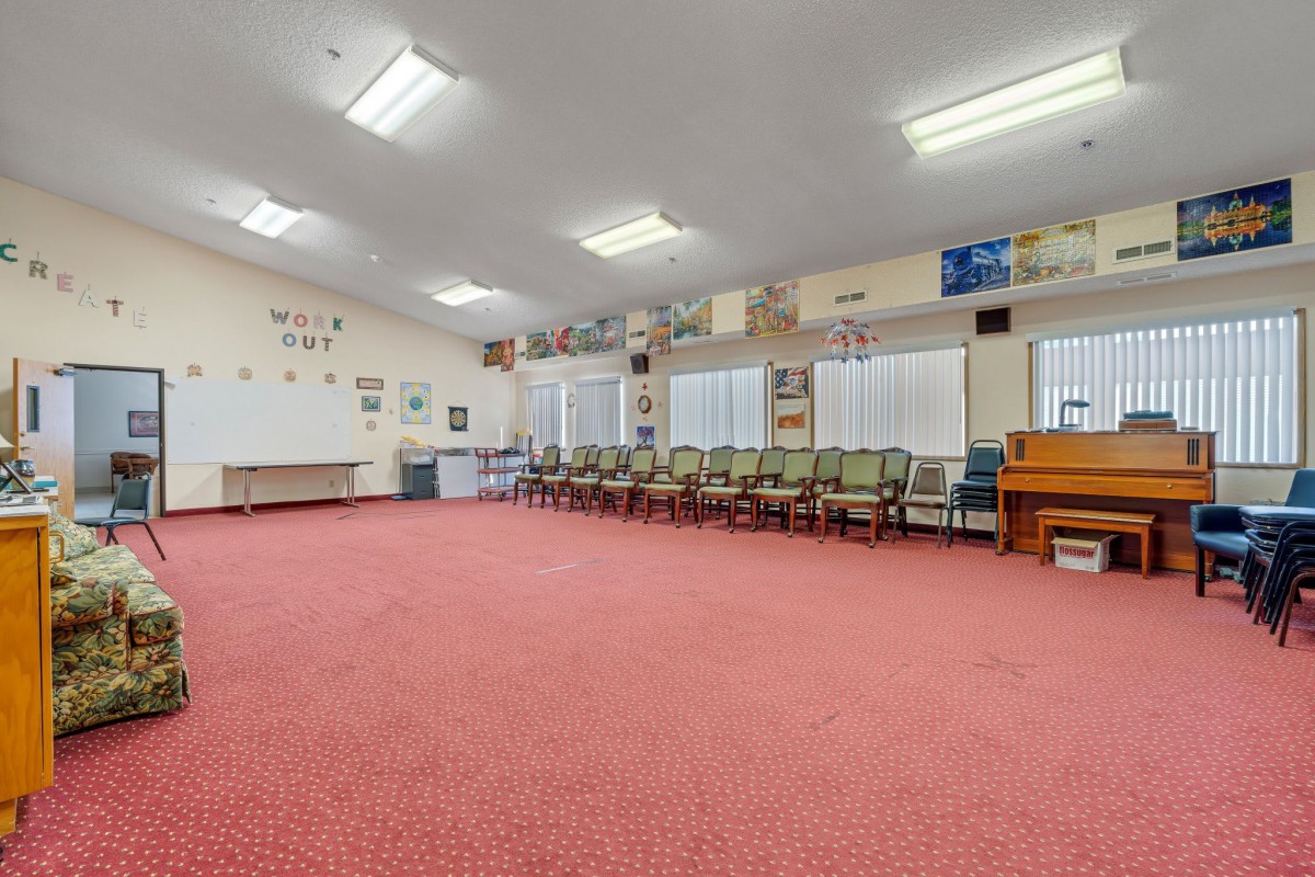 A spacious classroom with red carpet, lined with chairs and a piano.