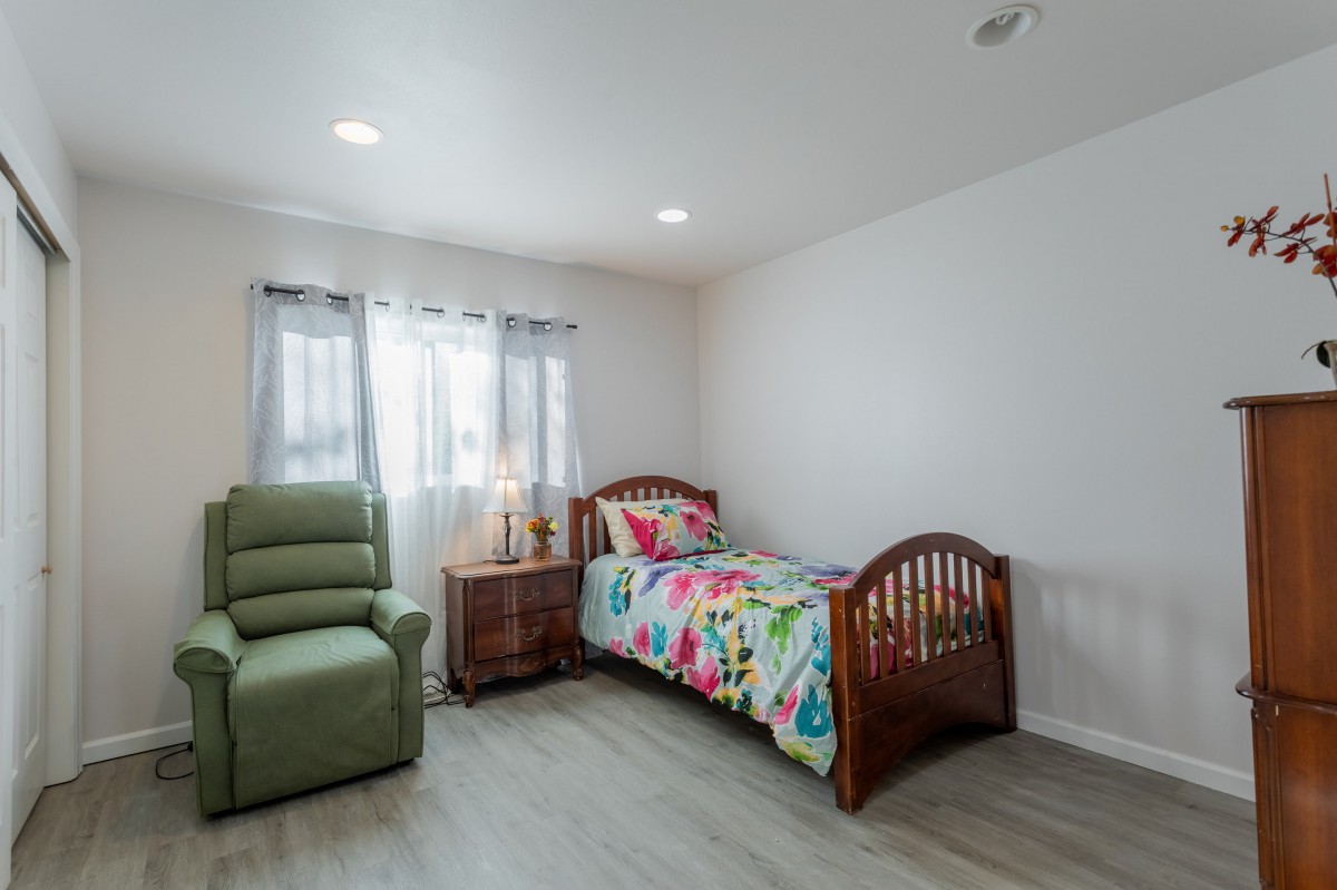 A cozy bedroom with a single bed featuring colorful bedding, a green armchair, and a wooden nightstand.