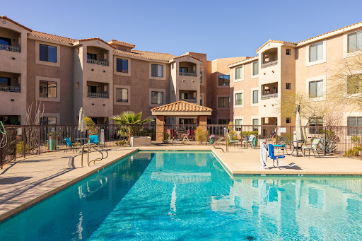 A relaxing residential area featuring a swimming pool surrounded by apartment buildings under a clear blue sky.