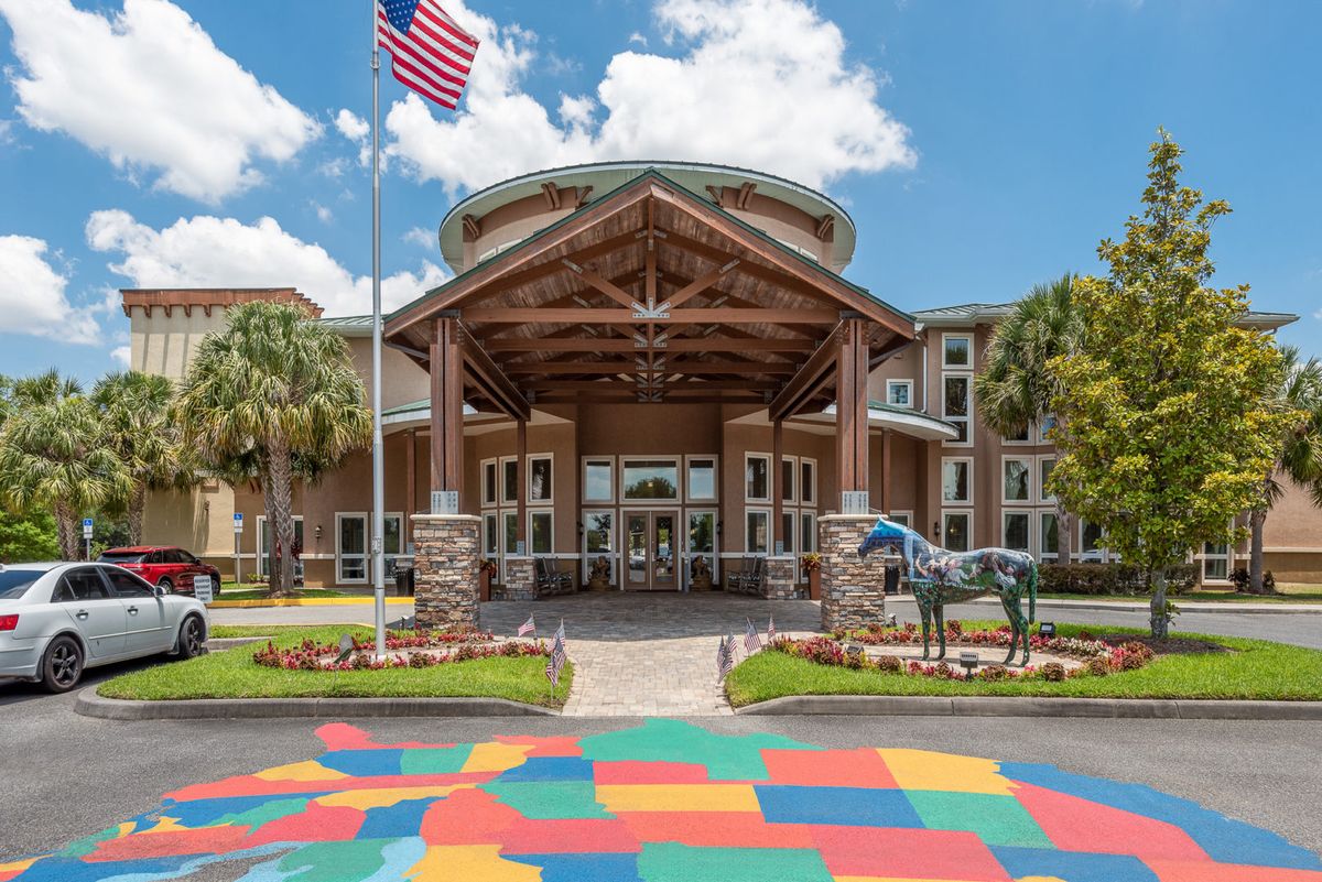 An entrance to a building with wooden accents, an American flag, and a statue on a colorful pavement.