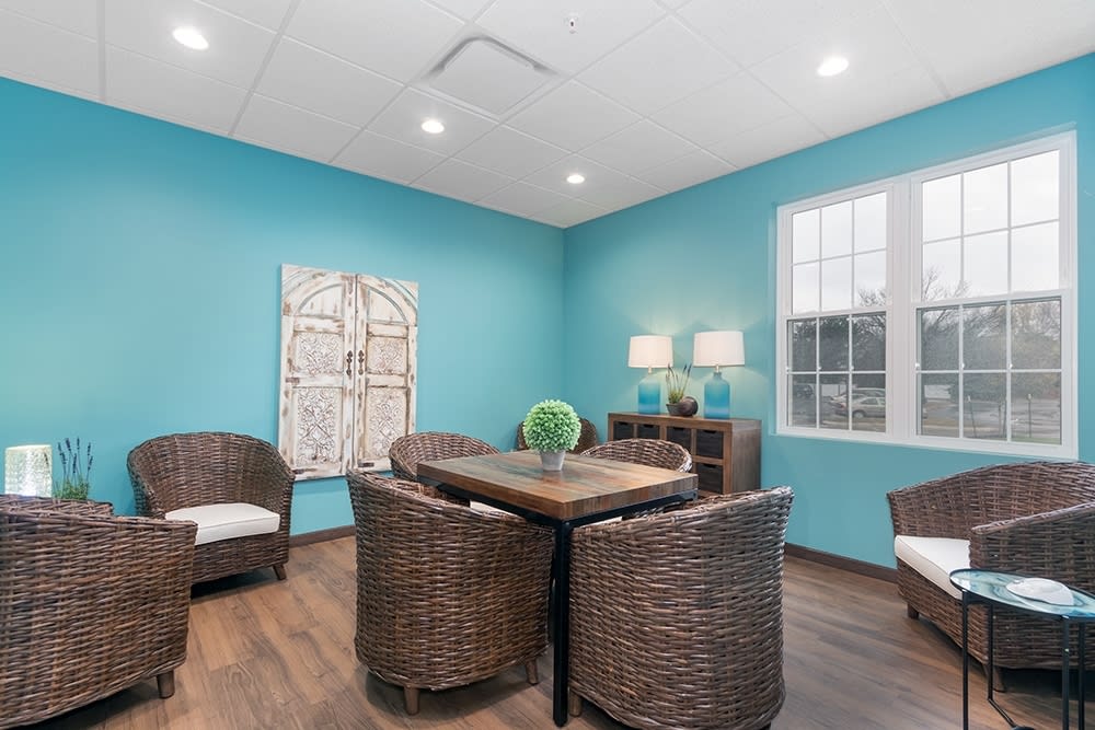 A cozy seating area with wicker chairs and a wooden table, accented by a blue wall and decorative artwork.