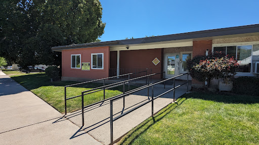 A building featuring a wheelchair-accessible ramp, surrounded by lush green grass under a clear blue sky.
