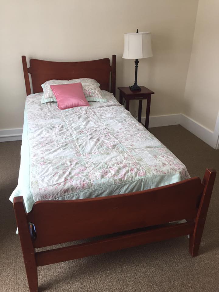 A single bed with a floral bedspread and pink pillow next to a nightstand and lamp.