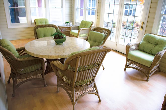 A sunlit dining area with wicker chairs featuring green cushions and a round table.