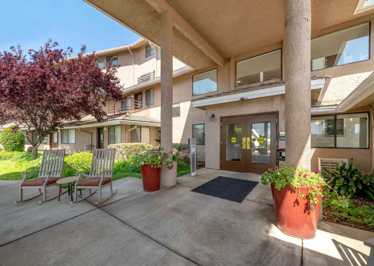 A sunny entrance of a building with potted plants and seating area.
