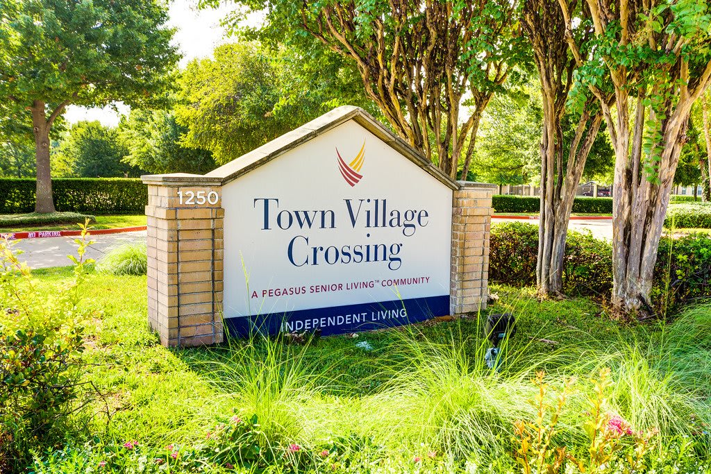 Entrance sign for Town Village Crossing, a retirement community, surrounded by greenery.