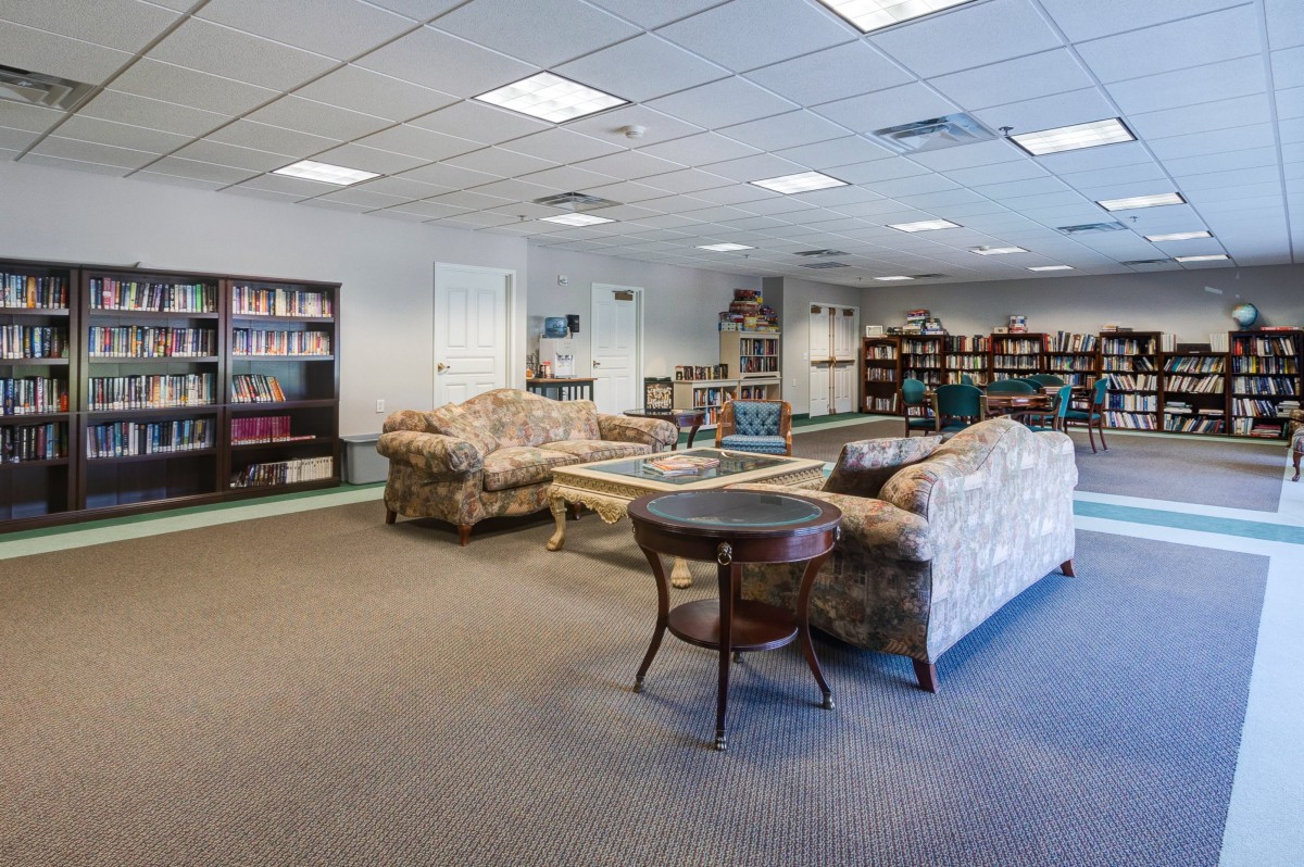 A cozy library space with bookshelves, sofas, and tables arranged for reading.