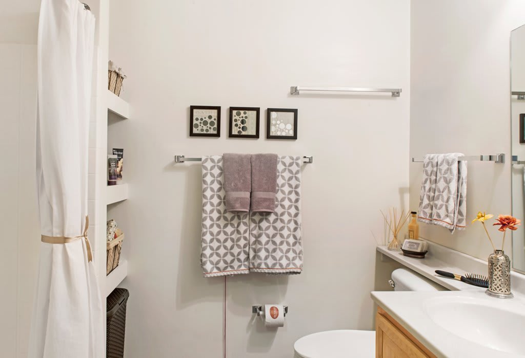 A neatly organized bathroom with patterned towels, wall art, and shelving.