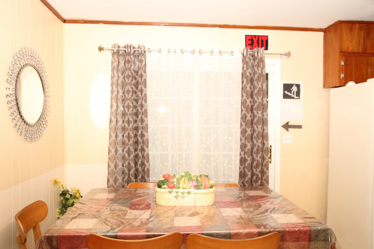 A dining area with a fruit basket on the table, patterned curtains, and a window.