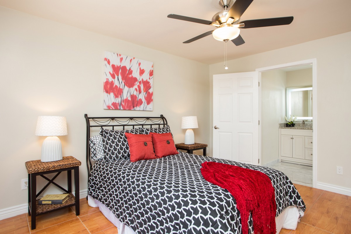 A modern bedroom featuring a stylish bed with patterned bedding and bold red accents, complemented by wooden nightstands and a ceiling fan.