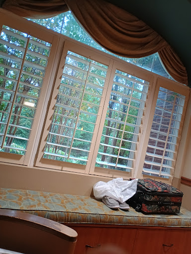 A cozy sitting area featuring large windows with wooden blinds, letting in natural light and a view of the greenery outside.