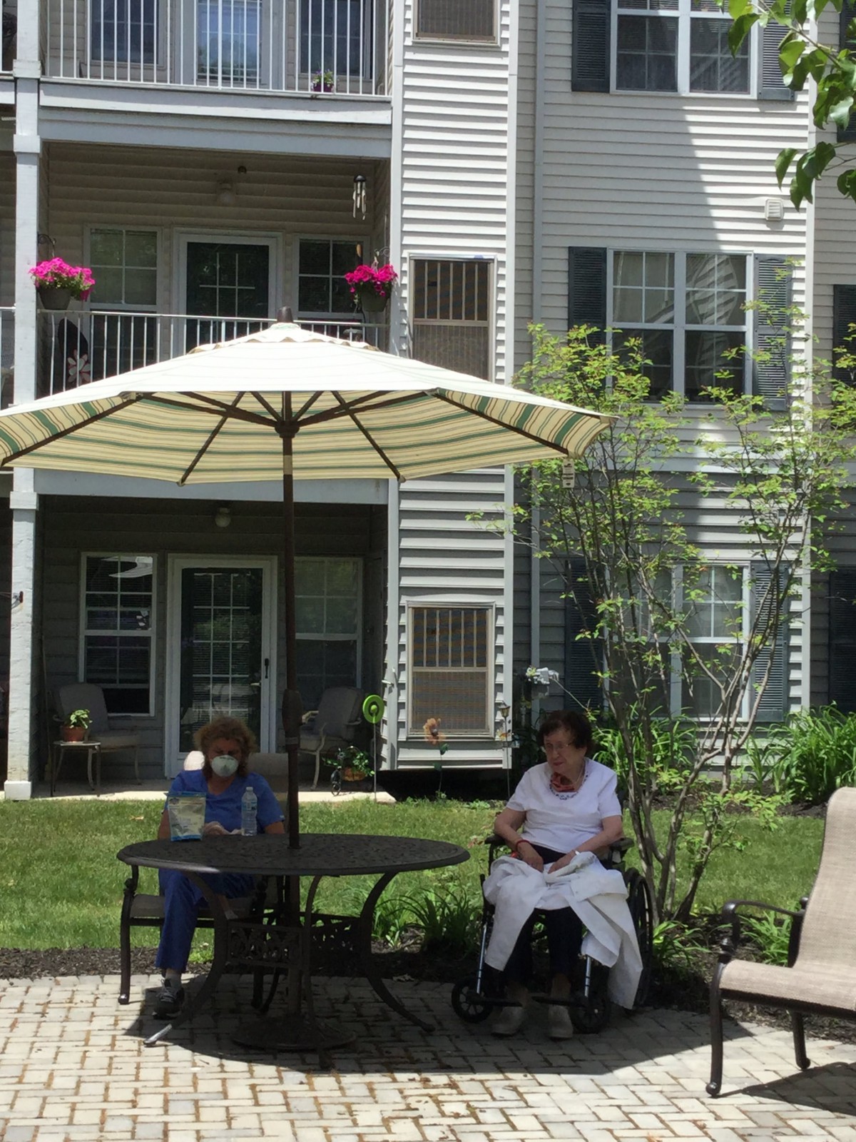 Two people sitting outside under an umbrella in a garden area of an apartment complex.