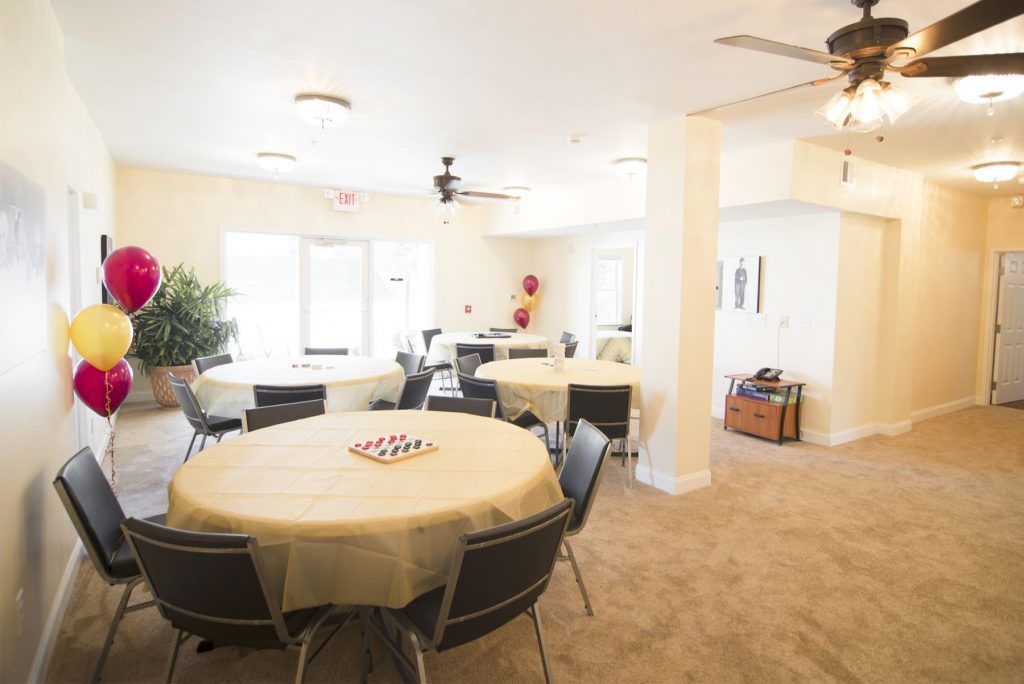 A spacious banquet hall setup with round tables and chairs, carpeted flooring, and ceiling fans.