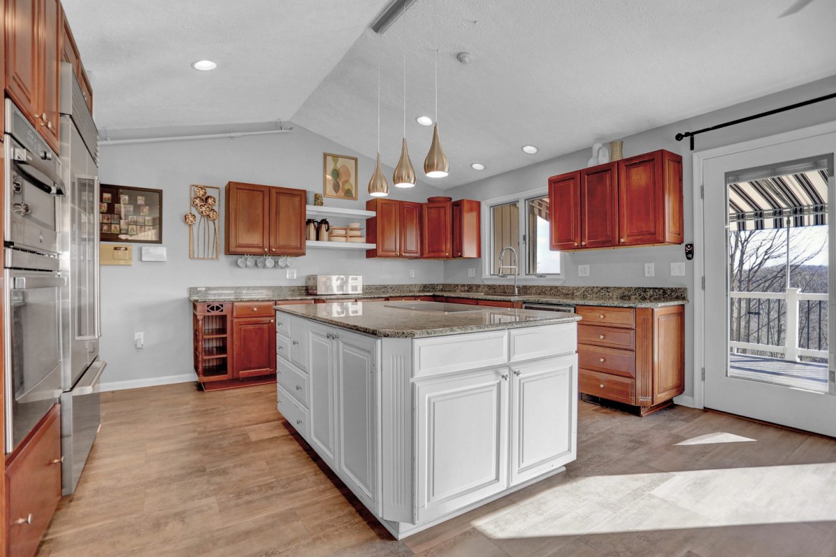 A modern kitchen featuring a large island with white cabinetry, surrounded by wood cabinets and illuminated by pendant lights.