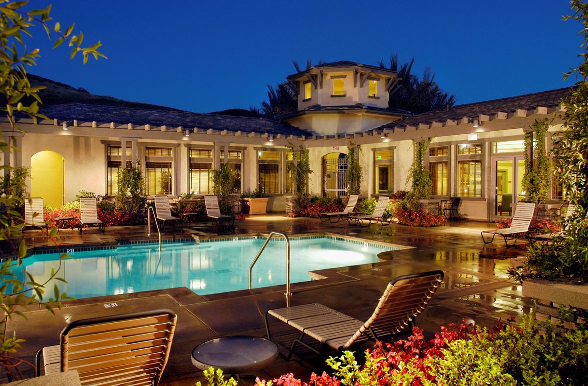 A luxurious house with a beautifully lit pool area at night.