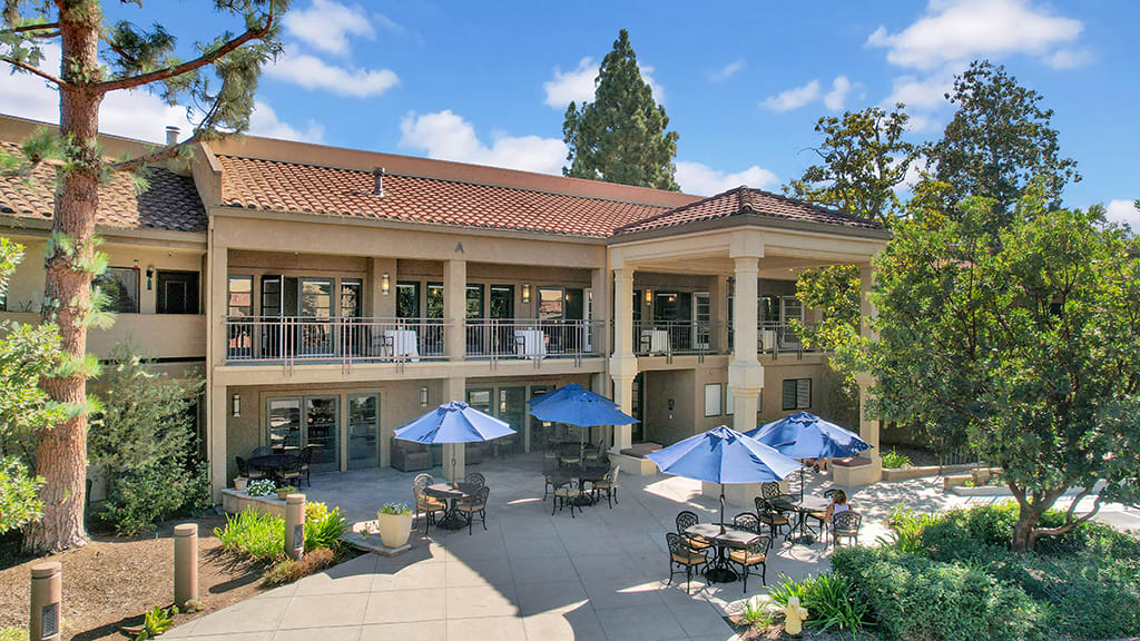 A scenic view of a modern building with outdoor seating and umbrellas on the patio.