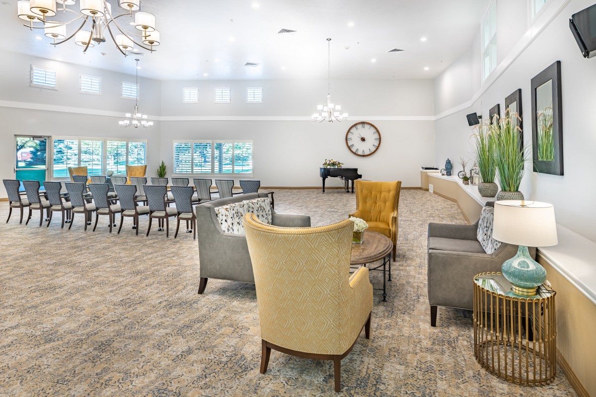 A spacious and elegant living room with modern furniture, featuring a seating area, piano, and large wall clock.