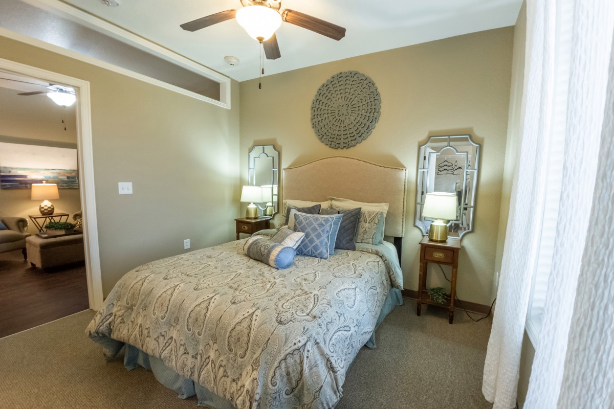 A cozy bedroom with a neatly made bed, decorative pillows, and stylish mirrors on either side.