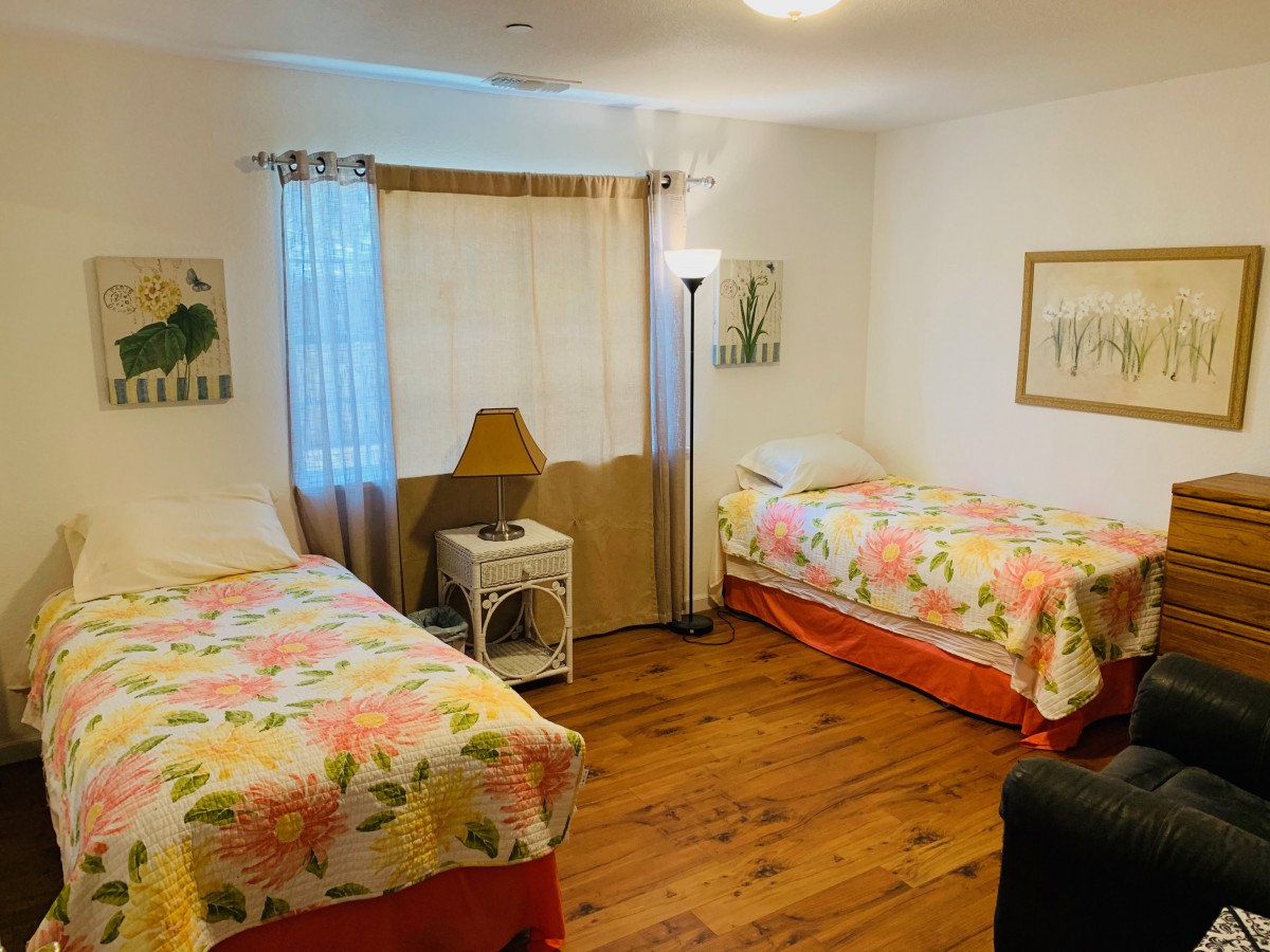 A cozy bedroom with two floral-patterned beds, wooden flooring, and decorative artwork.