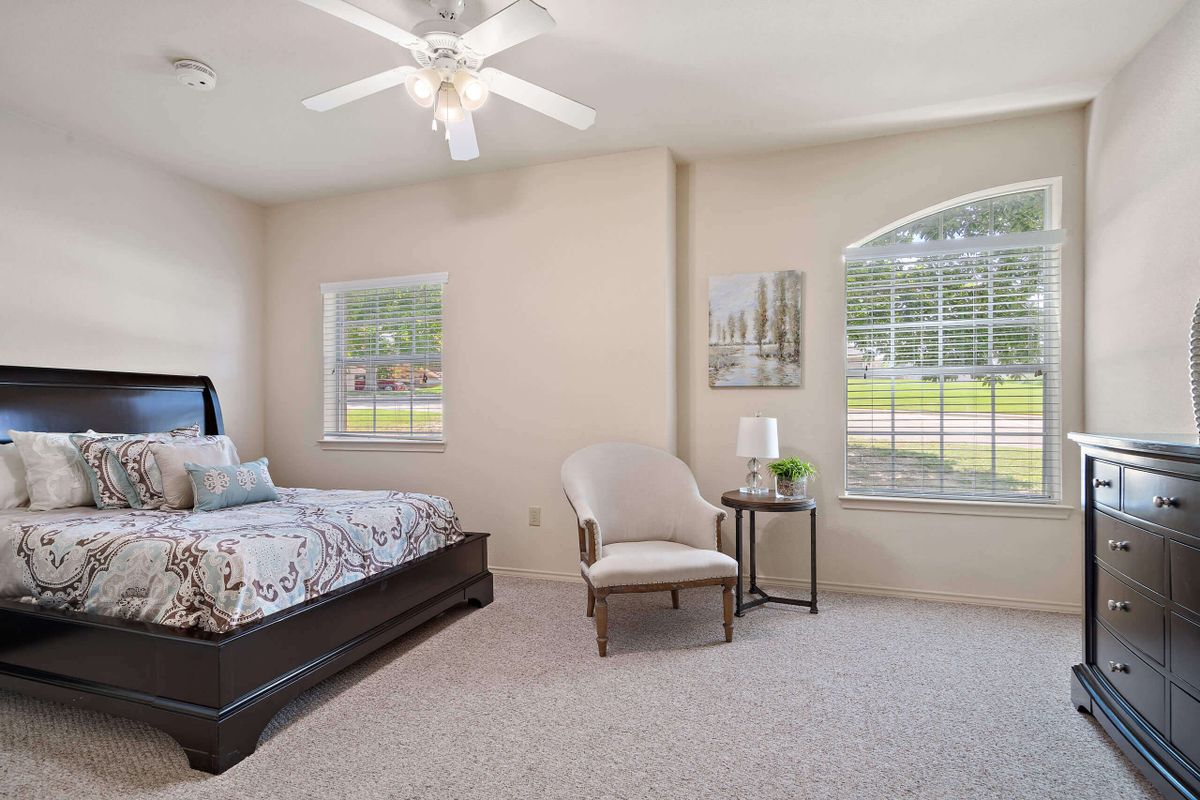 A cozy bedroom featuring a single bed, chair, and large windows with plenty of natural light.