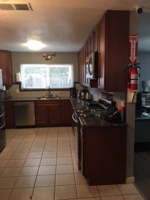 A modern kitchen with wooden cabinets, stainless steel appliances, and a tiled floor.