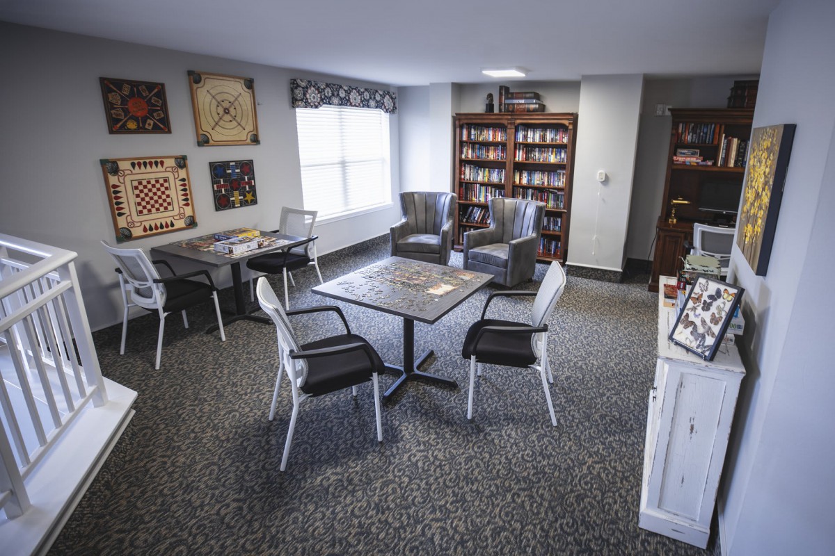 A cozy library room with tables, chairs, and bookshelves filled with books.