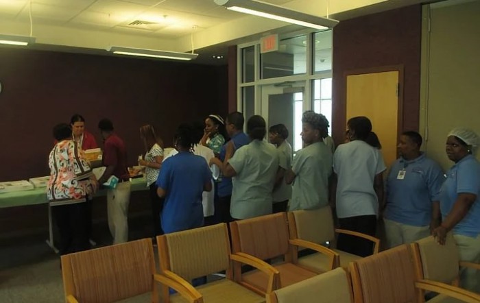 A group of people standing in line indoors, with chairs visible in the foreground.