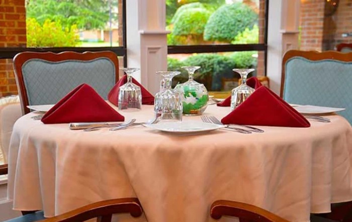 A beautifully set dining table with red napkins and elegant glassware near a window overlooking a garden.