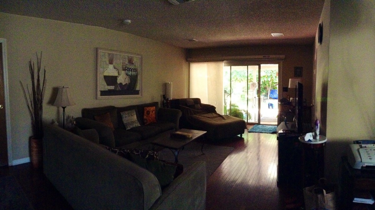 A cozy living room with a large sectional sofa, a coffee table, and artwork on the wall. Natural light streams in through a sliding glass door.