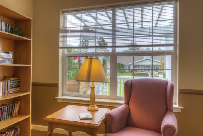A cozy living room with an armchair by the window, illuminated by a warm table lamp.