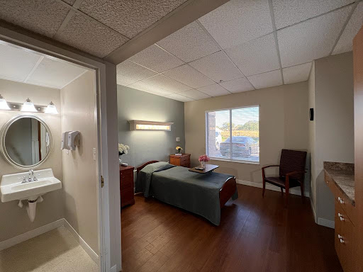 A well-lit hospital room featuring a bed, private bathroom, and seating area.