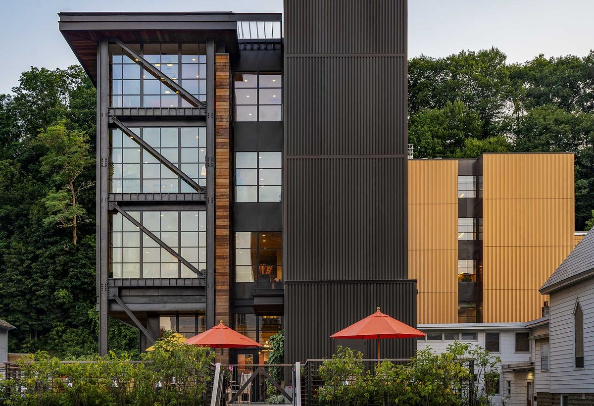 A modern urban building with large windows and patio umbrellas in front.