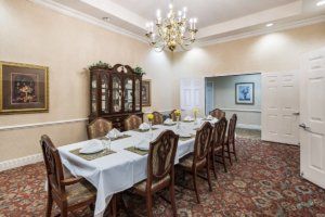An elegant dining room with a large table, upholstered chairs, and a chandelier.