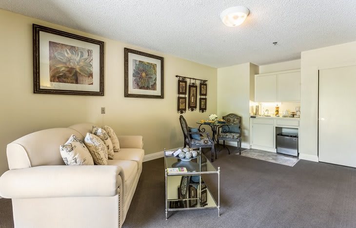A cozy living space with a sofa, dining table, and kitchenette, decorated with framed artwork.