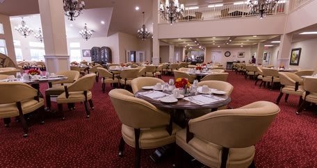 An elegantly set dining area with round tables and comfortable chairs, adorned with chandeliers overhead.