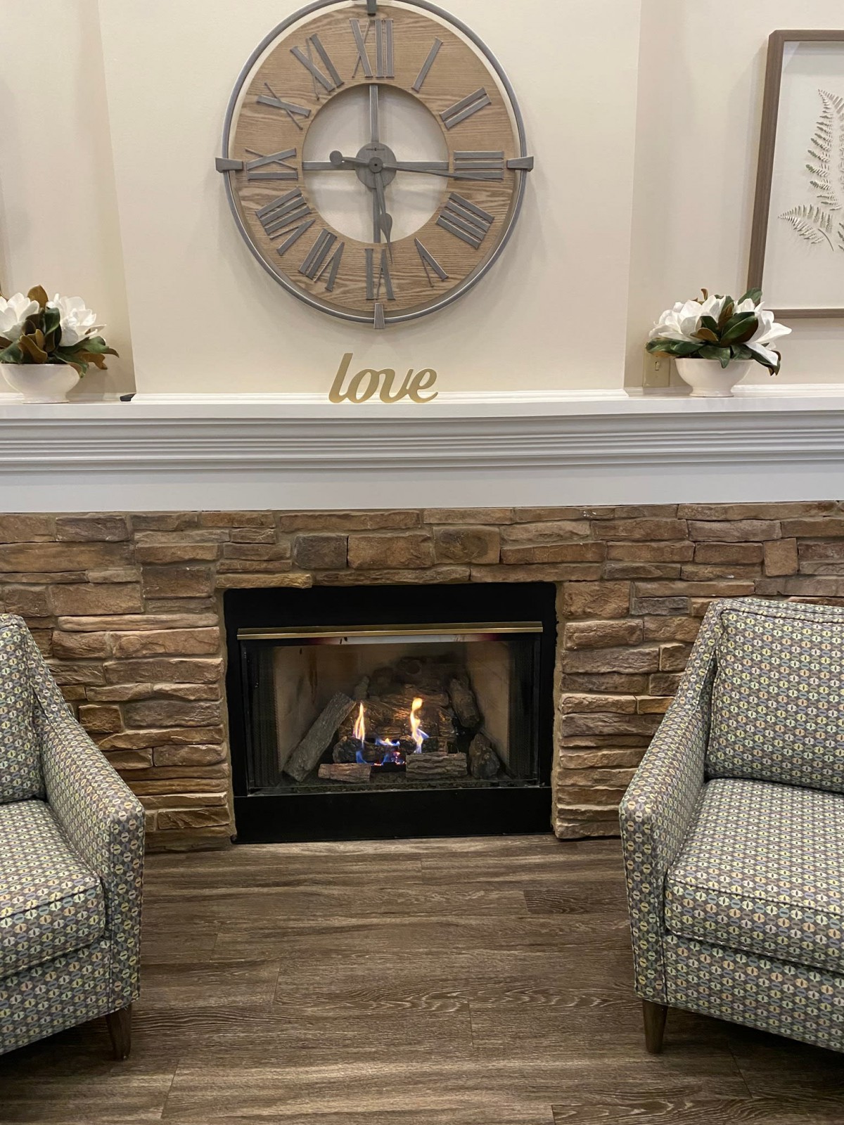 A cozy living room setting featuring a stone fireplace with two patterned chairs and decorative accents.