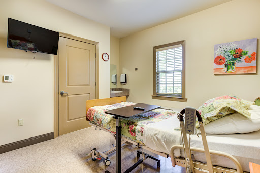 A well-lit patient room in a hospital featuring a bed, television, and window.
