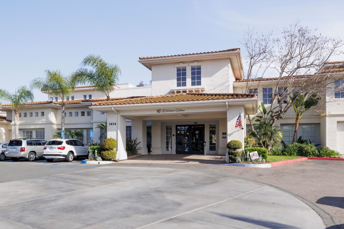 A sunny view of a building entrance with palm trees and parked cars.