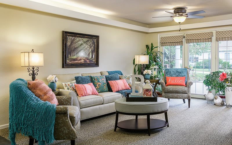 A cozy living room featuring a comfortable sofa and armchairs with colorful cushions, a coffee table, and a decorative painting on the wall.