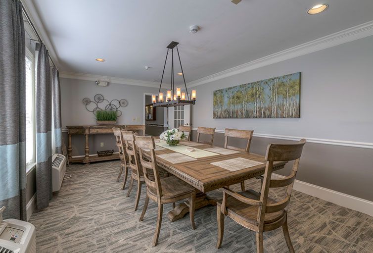 A spacious dining room featuring a long wooden table with matching chairs, illuminated by a chandelier. The room is decorated with wall art and plants, creating a cozy and elegant atmosphere.