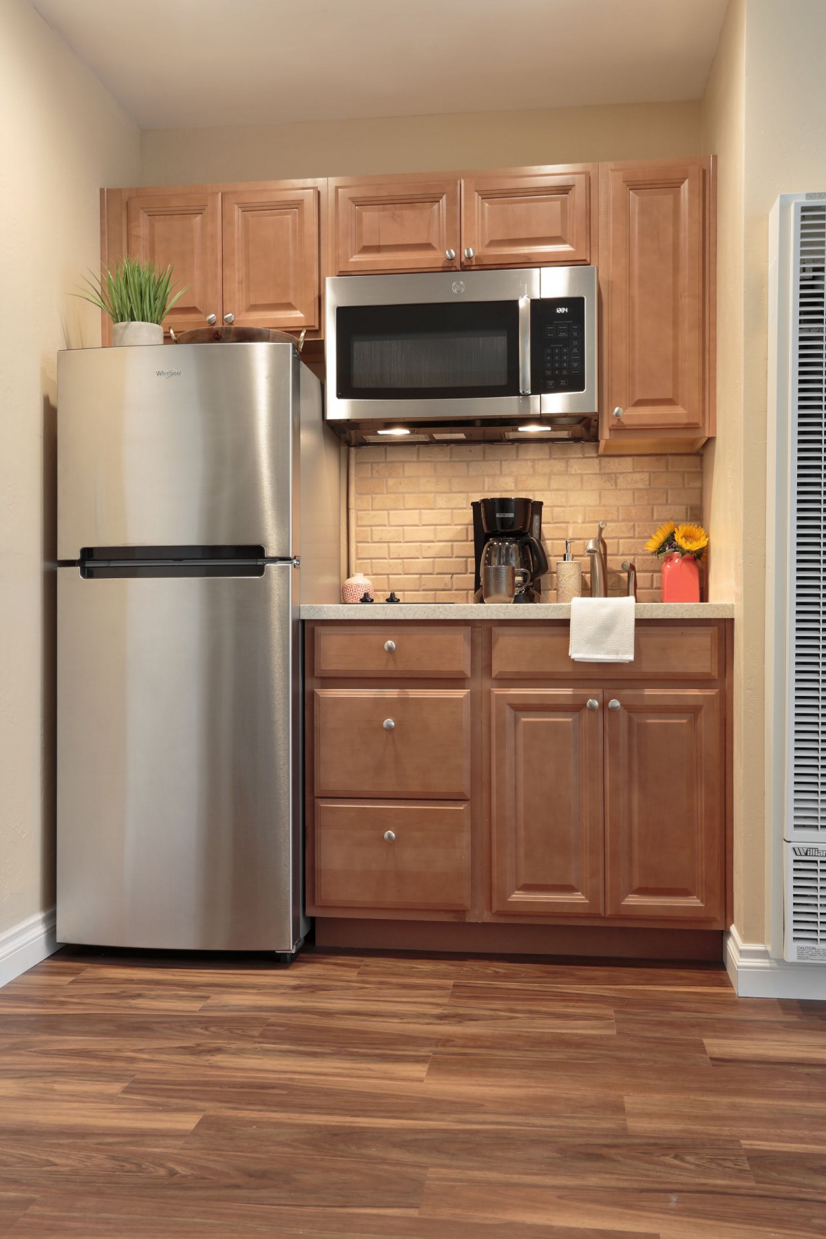 A compact kitchen setup with a refrigerator, microwave, and wooden cabinets.