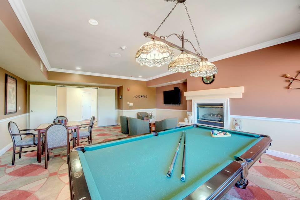A cozy recreation room featuring a pool table, chandelier lighting, fireplace, and a seating area with a television.