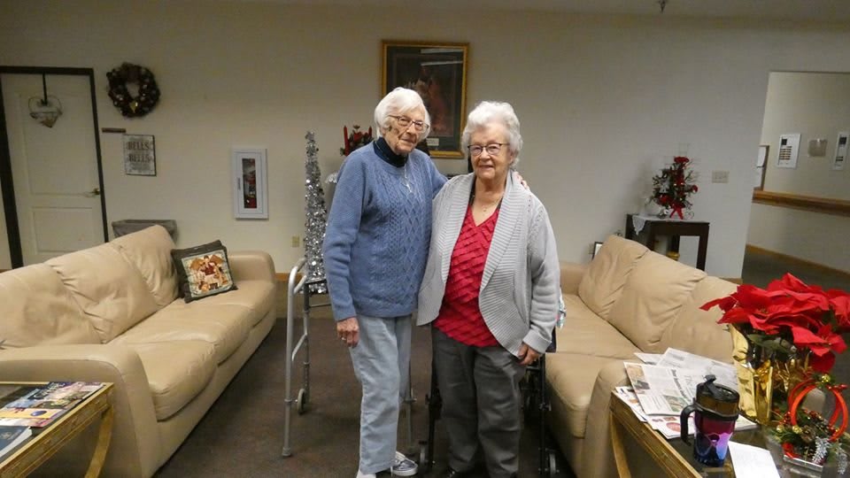 Two elderly women standing together in a living room, showcasing friendship and warmth.