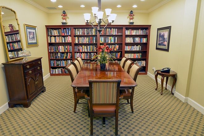 A formal library room with a central table surrounded by chairs and flanked by bookshelves.