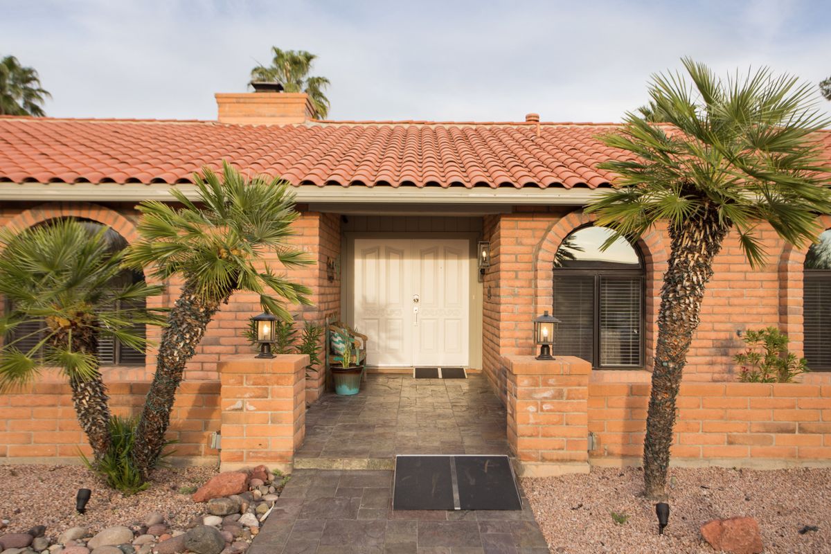 A brick house with a tiled roof and palm trees at the entrance.