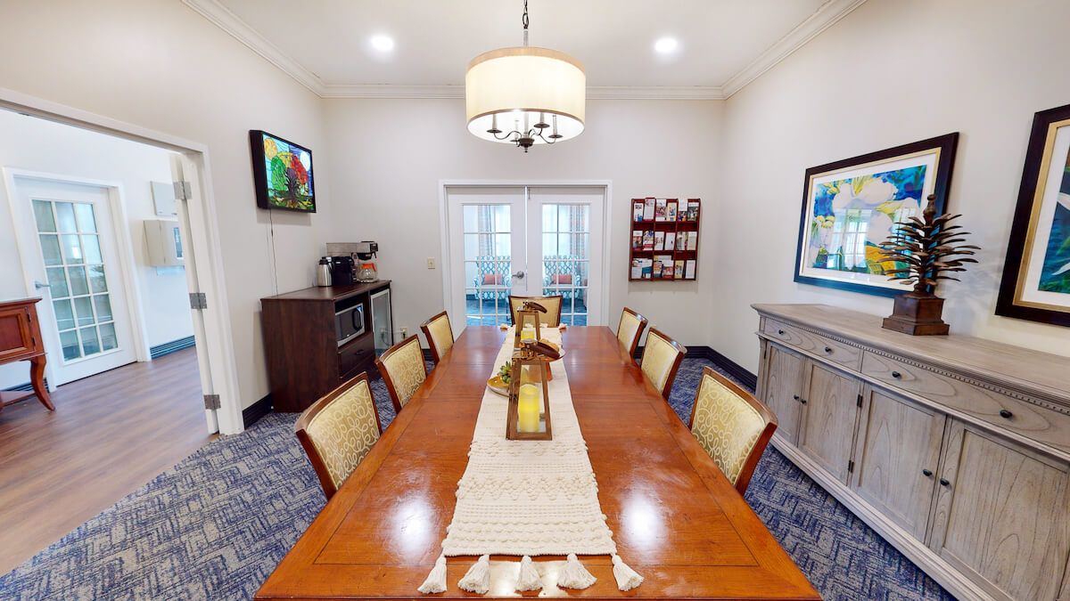 A modern dining room with a long table, surrounded by chairs, and illuminated by a chandelier.
